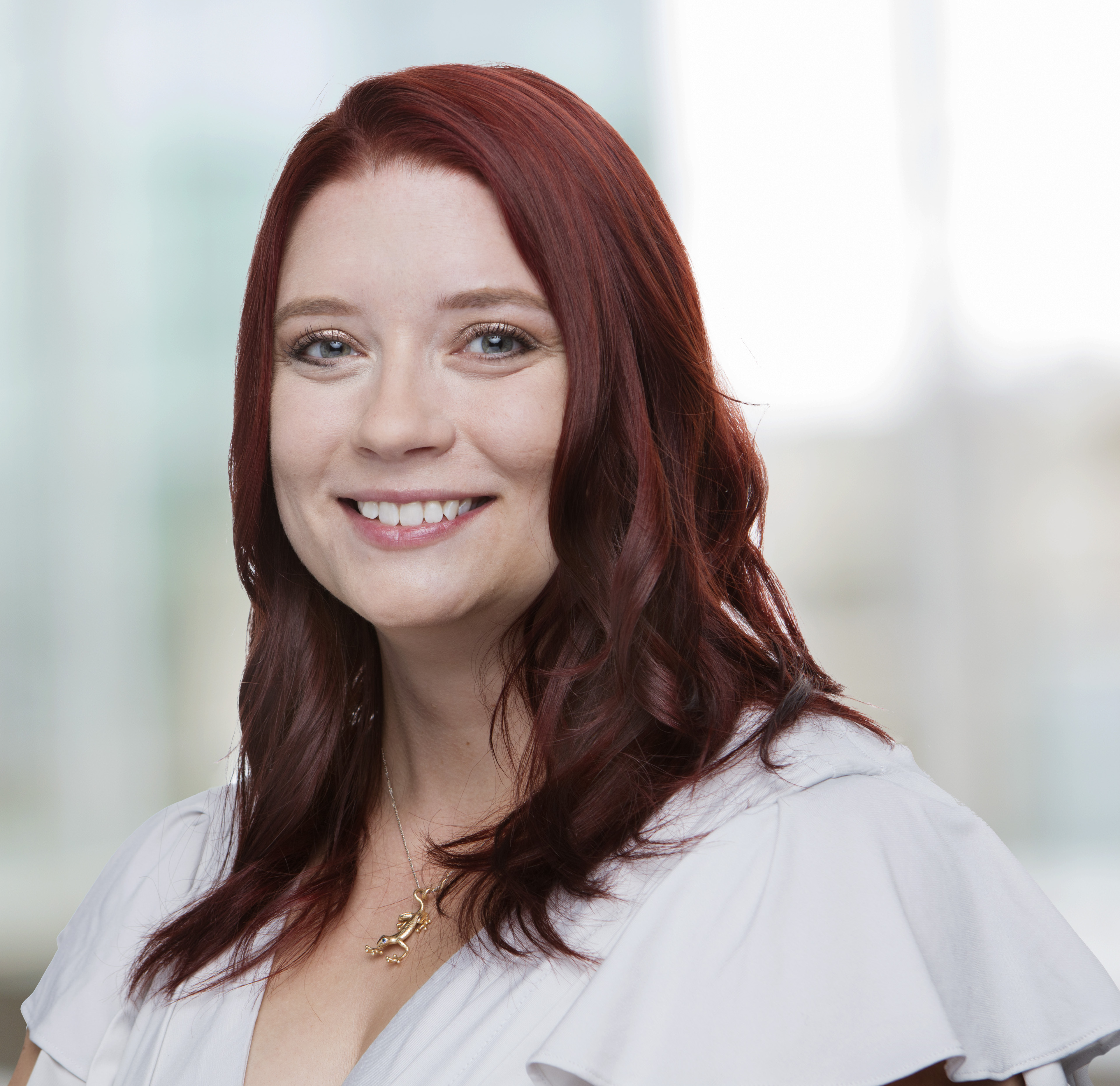 Headshot of a smiling woman in a white ruffled top with fair skin and burgundy hair.